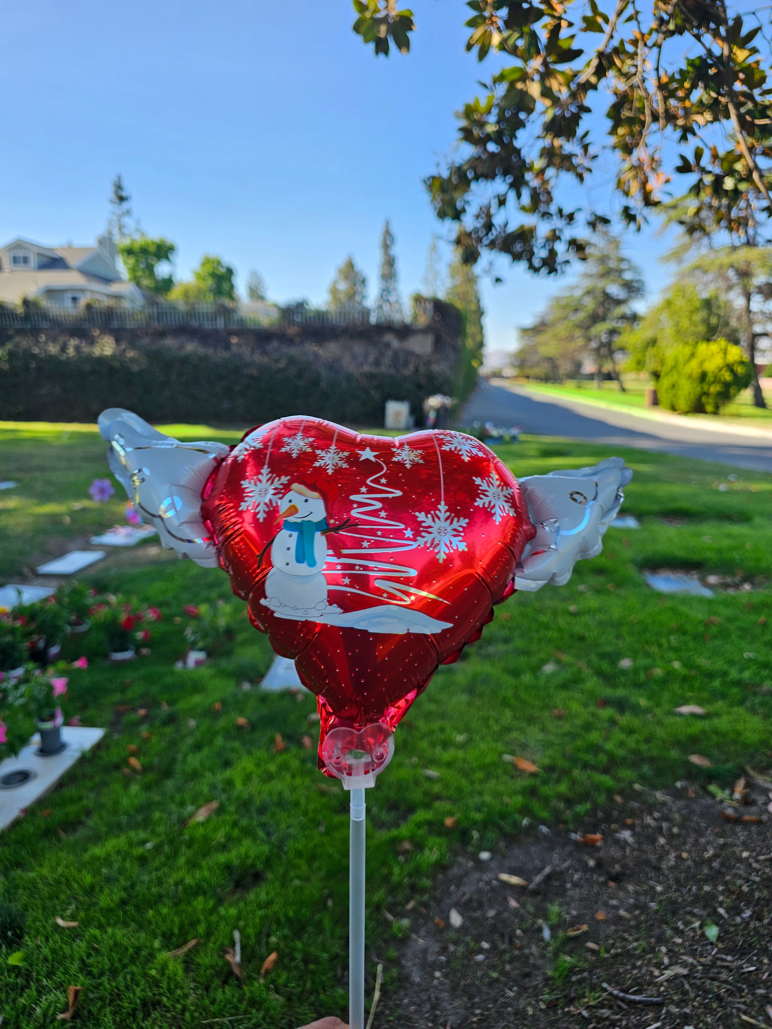 Christmas Snowman Memorial Balloon on a Stick with Angel Wings placed at a cemetery graveside